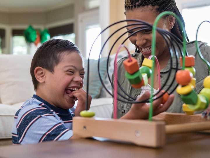 Mom and son with Down syndrome laugh together while playing in living room.