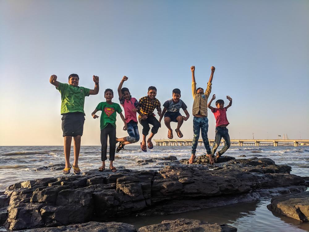 Group of children joyfully jumping up from rocks on the beach.