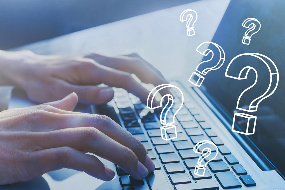 Hands typing on a laptop with question mark elements in front of the laptop screen