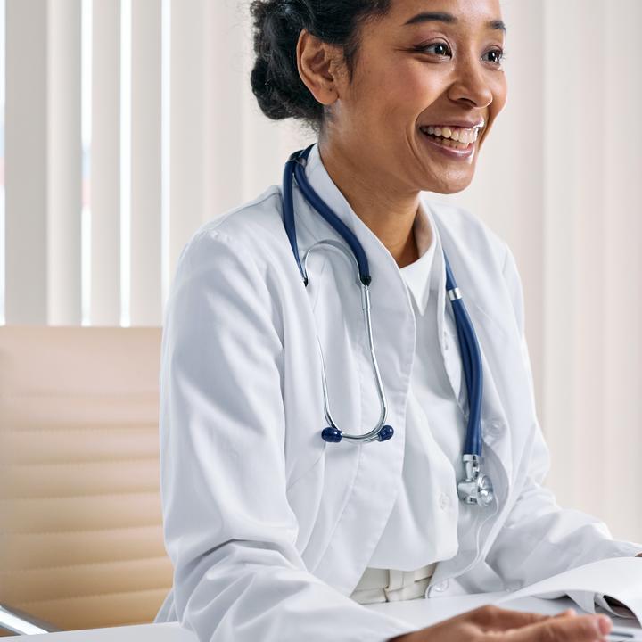 Woman doctor in white lab coat and stethoscope smiling at person off camera.